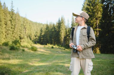 Mutlu çocuk yaz tatilinde ormanda fotoğraf çekiyor, doğanın güzelliğinin tadını çıkarıyor.