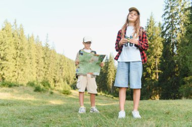 İki genç yürüyüşçü bir ormanı keşfediyor, biri harita tutuyor diğeri dürbün kullanıyor.
