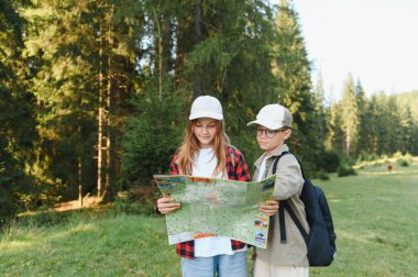 İki genç yürüyüşçü yemyeşil bir ormanda açık hava maceralarının tadını çıkarırken haritaya danışıyorlar.