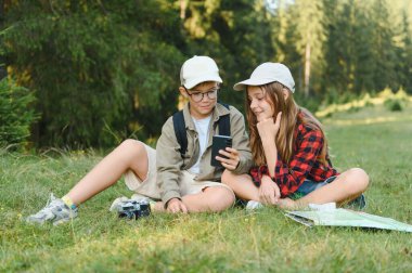İki genç izci ormanda oturuyorlar, akıllı telefon ve harita kullanıyorlar, açık hava maceraları sırasında teknolojiyi ve geleneksel navigasyonu birleştiriyorlar.