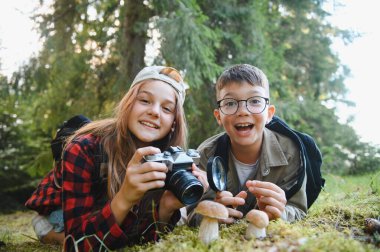 İki genç turist ormanda çimlerin üzerinde uzanmış yürüyüş sırasında mantarları inceliyor ve resimlerini çekiyorlar.