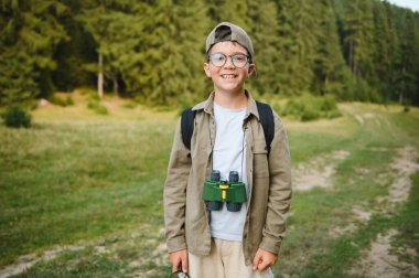 Dürbün ve büyüteçle donatılmış, doğayı keşfeden ve dışarıda eğlenen meraklı çocuk ormanda yürüyüş yapıyor.