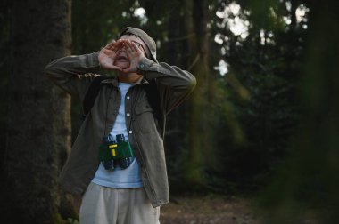Dürbün ve sırt çantası takan genç izci yoğun bir ormanda kaybolduktan sonra yardım için bağırıyor.