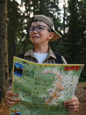 Genç izci gözlüklü ve beyzbol şapkalı, elinde bir harita ve ağlayan, yoğun bir ormanda kaybolmuş ve kafası karışmış hisseden.