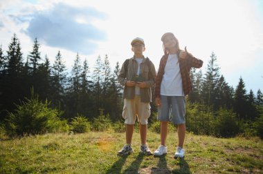 Ormanda güneşli bir günün tadını çıkaran iki genç yürüyüşçü. Biri pusula tutuyor, diğeri de onay veriyor.