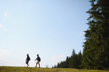 İki genç yürüyüşçü, güneşli bir günde doğanın güzelliğini kucaklayarak yaz ormanlarında manzaranın tadını çıkarıyorlar.