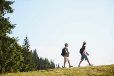 Sırt çantalı iki genç yürüyüşçü güneşli bir ormanda yürüyüş yaparak aktif ve sağlıklı bir yaşam tarzını destekliyor.