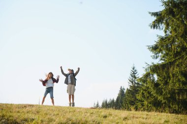 Sırt çantalı iki genç turist bir dağ manzarasına atlayıp yürüyüş sırasında neşelerini dile getiriyorlar.