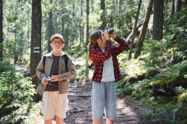 İki genç yürüyüşçü yemyeşil bir ormanı keşfediyor. Dürbün kullanan kız, elinde kamera, açık hava maceralarının tadını çıkarıyor.