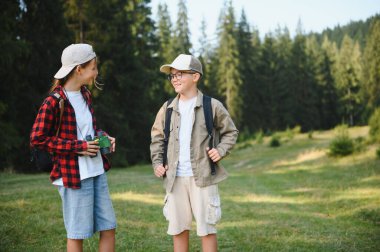 Sırt çantalı iki genç yürüyüşçü açık hava macerasının tadını çıkarıyorlar, yemyeşil bir ormanın canlı yeşiliyle çevrili, gülümseyen ve keşfeden