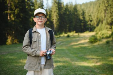 Sırt çantası ve kamerası olan genç bir turist yemyeşil bir ormanda yürüyüş yapıyor, doğanın güzelliğini ve macerasını kucaklıyor.