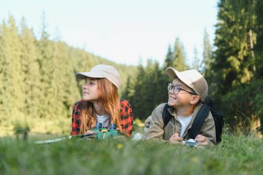 İki genç turist yemyeşil çimlerin üzerinde uzanmış yürüyüş maceralarının tadını çıkarırken nefes kesen dağ manzarasında sırılsıklam oluyorlar.