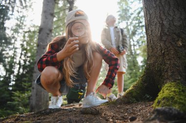 Çocuklar ormanda doğayı keşfeder, büyüteç ve dürbün kullanır, yaz tatilinde çevreyi öğrenirler.