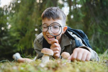 Ormanı keşfeden meraklı çocuk yürüyüş sırasında büyüteçle mantar gözlemliyor.