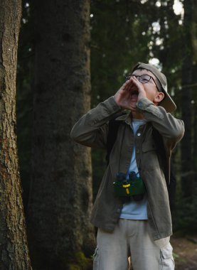 Dürbün ve sırt çantası takmış, ormanda yüksek sesle bağıran çocuk, muhtemelen kayboldu ya da yardım istiyor.