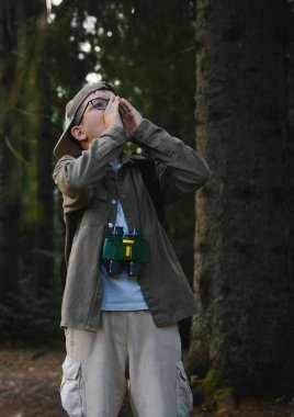 Dürbün ve sırt çantası takan genç bir izci, ağaçlarla dolu sık bir ormanda yol alırken yardım için bağırıyor.