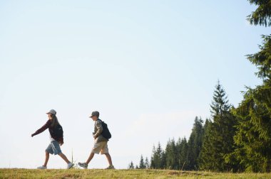 Güneşli bir günde dağlarda yürüyen genç yürüyüşçüler güzel manzaranın ve temiz havanın tadını çıkarıyorlar.