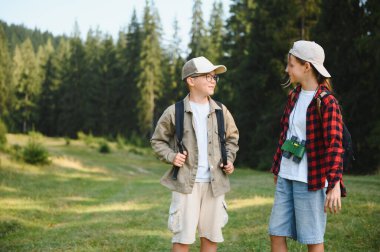 İki genç izci, zengin bir ormanda gezintiye çıkıyor. Sırt çantaları ve dürbünlerle donatılmış, macera ve keşfe hazır.