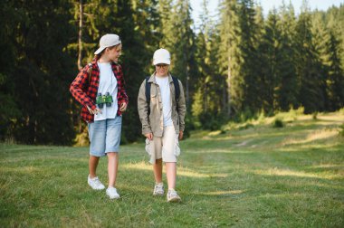 Sırt çantalı ve dürbünlü iki genç yürüyüşçü yemyeşil bir ormanda yürüyüş yapıyor.