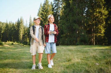 İki genç izci, yemyeşil bir ormanda gezintiye çıkıyorlar. Sırt çantaları ve dürbünle donatılmış, maceraya hazır.