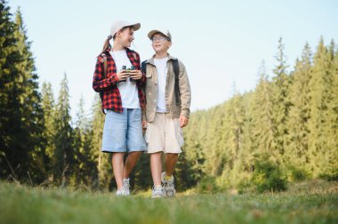 Sırt çantalı ve dürbünlü iki genç yürüyüşçü yemyeşil bir ormanda yürüyorlar, açık hava maceraları sırasında doğanın güzelliğinin tadını çıkarıyorlar.