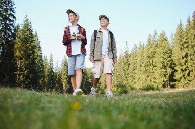 Canlı yeşil bir ormanda yürüyüş yapan iki genç izci macera dolu keyifli bir yaz gününde güneşin tadını çıkarıyorlar.