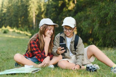 Erkek ve kız izciler, verimli bir ormanda yürüyüş yaparken yön bulmak için akıllı telefon kullanıyorlar. Doğanın ve keşiflerin tadını çıkarıyorlar.