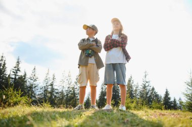 Dürbünlü iki genç yürüyüşçü, açık hava maceraları sırasında güvenli bir şekilde ormanlık alanda durup manzaranın tadını çıkarıyorlar.