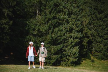 İki genç turist el ele tutuşuyor ve yemyeşil bir ormanda yürüyüş yapıyor, doğa ile çevrili tatillerinin tadını çıkarıyorlar.