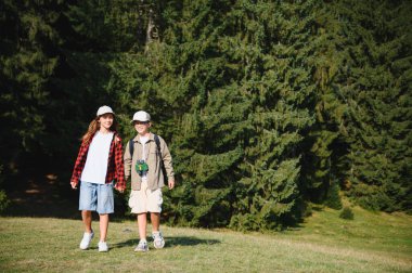 İki genç yürüyüşçü, bir erkek ve bir kız, el ele tutuşuyorlar ve canlı yeşil ormanda manzaralı bir yolculuğa çıkıyorlar.