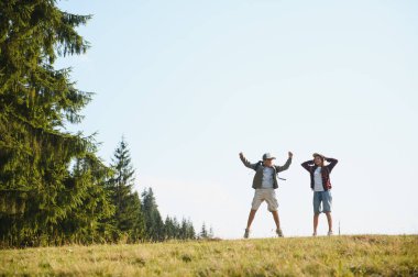 İki genç turist yaz tatilleri boyunca bir dağ manzarasında mutluluğu ve özgürlüğü ifade ederek zıplıyorlar.