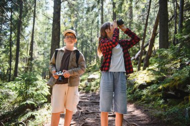 İki genç yürüyüşçü, elinde kamera olan bir oğlan ve dürbün kullanan bir kız yemyeşil orman patikalarını keşfederek doğanın harikalarından keyif alıyorlar.