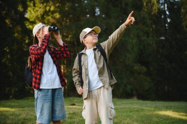 İki genç yürüyüşçü, bir erkek ve bir kız, doğayı keşfediyorlar, oğlan ilginç bir şeyi işaret ediyor ve kız dürbün kullanıyor.