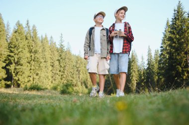 Ormanın kenarındaki çimenli bir arazide yürüyen iki genç yürüyüşçü, manzaranın tadını çıkarıyor ve kuşları izlemek için dürbün taşıyor.