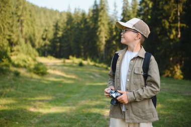 İzci çocuk ormanda yürüyüş yapmaktan ve kamerasıyla fotoğraf çekmekten zevk alıyor, doğanın güzelliğini kucaklıyor.