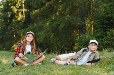 Genç turistler orman yürüyüşünden zevk alıyorlar, bir harita okuyorlar ve çimlerin üzerinde dinleniyorlar, macera ve keşfin neşesini kucaklıyorlar.