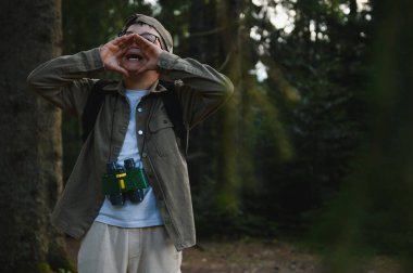 Yoğun bir ormanda yardım için bağıran, dürbün ve sırt çantası takan, macera ve keşif ruhunu somutlaştıran kayıp çocuk.