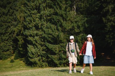 Yaz tatillerinde yemyeşil bir ormanda yürüyüş yapan iki genç turist el ele tutuşuyor.