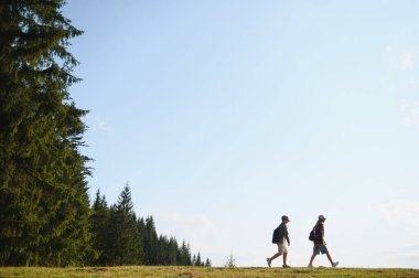 Güneşli bir yaz gününde canlı yeşil bir ormanda yürüyüş yapan iki genç izci doğanın ve maceranın neşesini kucaklıyor.