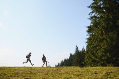 Güneşli bir günde dağda koşan iki turist güzel manzaranın ve temiz havanın tadını çıkarıyor.