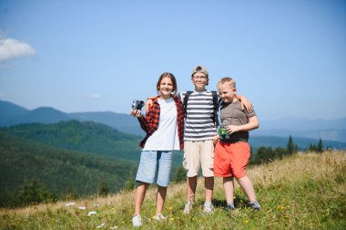 Üç genç yürüyüşçü bir dağın zirvesinde kucaklaşıp yaz tatili boyunca nefes kesici manzaranın tadını çıkarıyorlar.