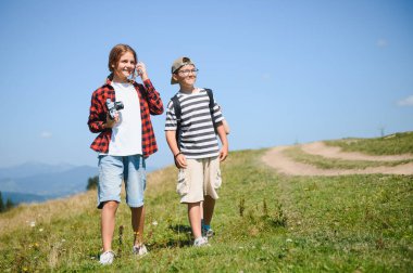Manzaralı bir dağ yolunda yürüyüş yapan iki çocuk açık havada güneşli bir günün tadını çıkarıyorlar. Gençlik keşfi ve maceranın mükemmel tasviri