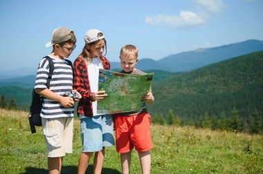 Dağlarda güneşli bir yaz gününün tadını çıkarırken, doğa ve birbirlerinin arkadaşlığından keyif alan üç genç yürüyüşçü harita çalışıyor.