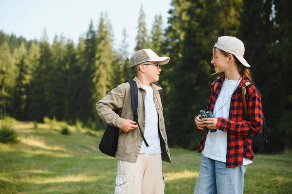 İki genç yürüyüşçü, bir oğlan ve bir kız sırt çantaları ve dürbünleriyle yemyeşil bir ormanda gezintilerinin tadını çıkarıyorlar.