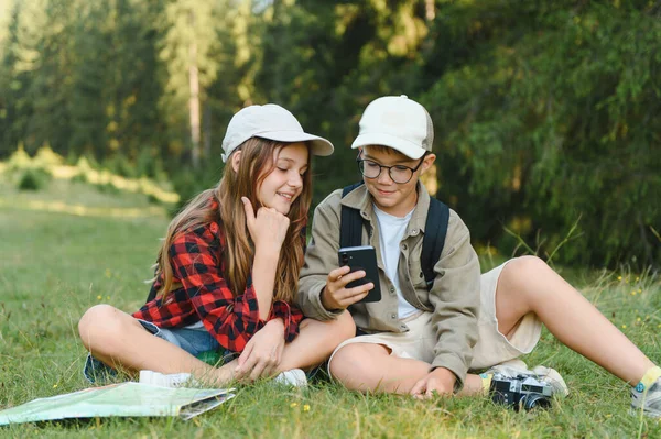 Erkek ve kız izciler, verimli bir ormanda yürüyüş yaparken yön bulmak için akıllı telefon kullanıyorlar. Doğanın ve keşiflerin tadını çıkarıyorlar.