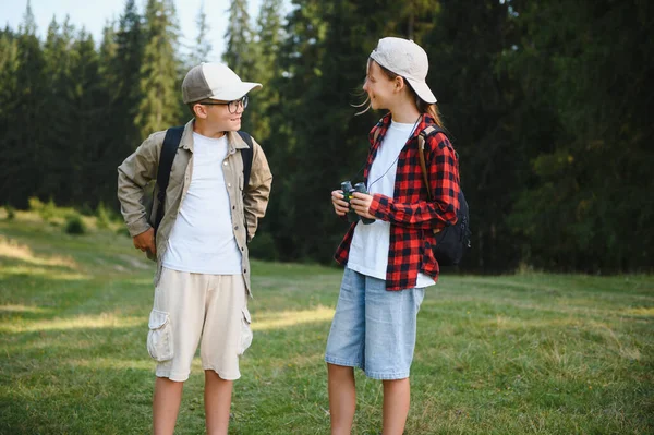 Sırt çantaları ve dürbünle donatılmış iki genç yürüyüşçü yaz kampı maceraları boyunca doğa yürüyüşünün tadını çıkarıyorlar.