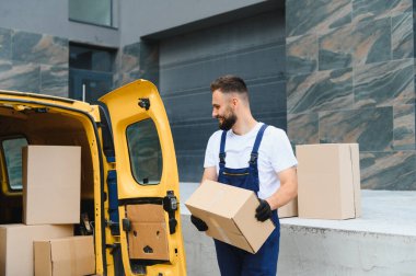 Gülümseyen teslimatçı, parlak sarı bir teslimat kamyonetinden karton kutuları indiriyor müşteri memnuniyeti için paketleri etkili bir şekilde tutuyor.