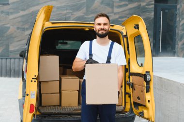 Kurye, teslimat minibüsünün yanında, kameraya gülümsüyor, nakliyeye ve taşımaya hazır.