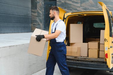Eldiven giyen kurye, işlek bir caddede çeşitli paketlerle dolu bir kamyonetten karton bir kutu taşıyor.