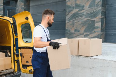 Kurye, parlak sarı bir teslimat kamyonundan karton kutuları indiriyor. Malları doğrudan müşterilerin kapısına taşıyor.